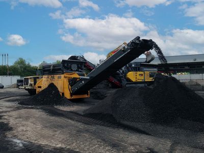 Anaconda FSL100 heavy-duty scalper stockpiling dark aggregate in a yard, other machines behind it