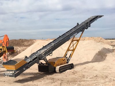 Anaconda TR75 tracked conveyor raised over sand piles, an excavator at the left edge