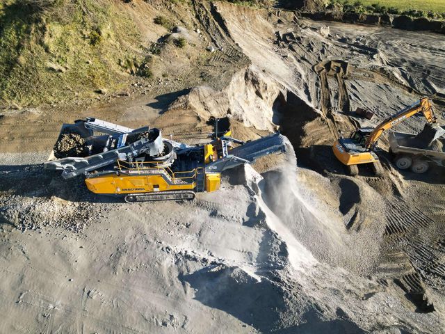 Anaconda C12 cone crusher working in a sand and gravel pit, an excavator loading a truck behind it