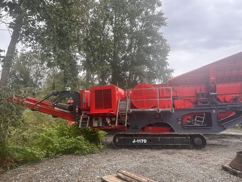 The 2018 J-1170 from the conveyor end, parked on gravel beside trees